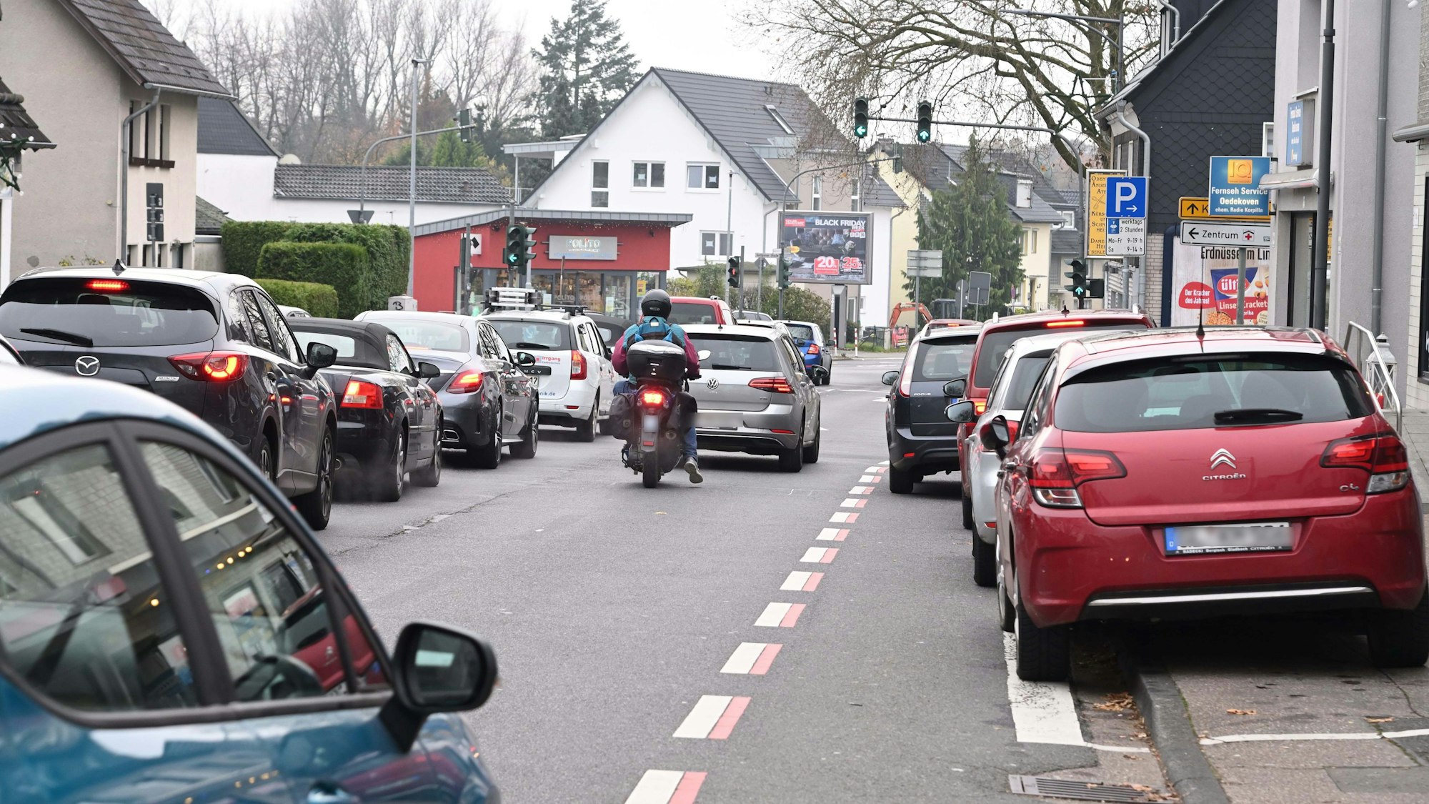 Autos stehen im Stau vor der Ampel. Rechts parken Autos entlang der Straße.