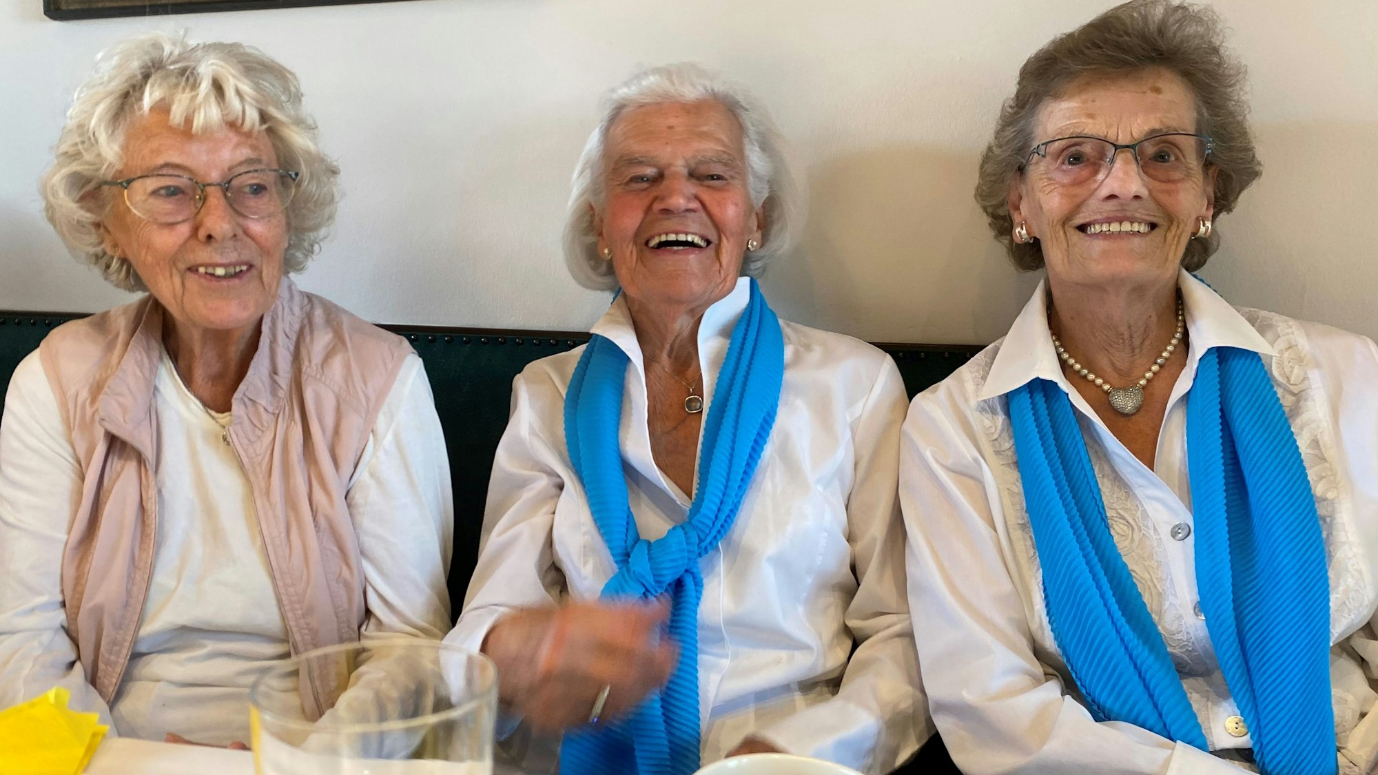 Drei ältere Frauen sitzen auf einer Bank und lachen.