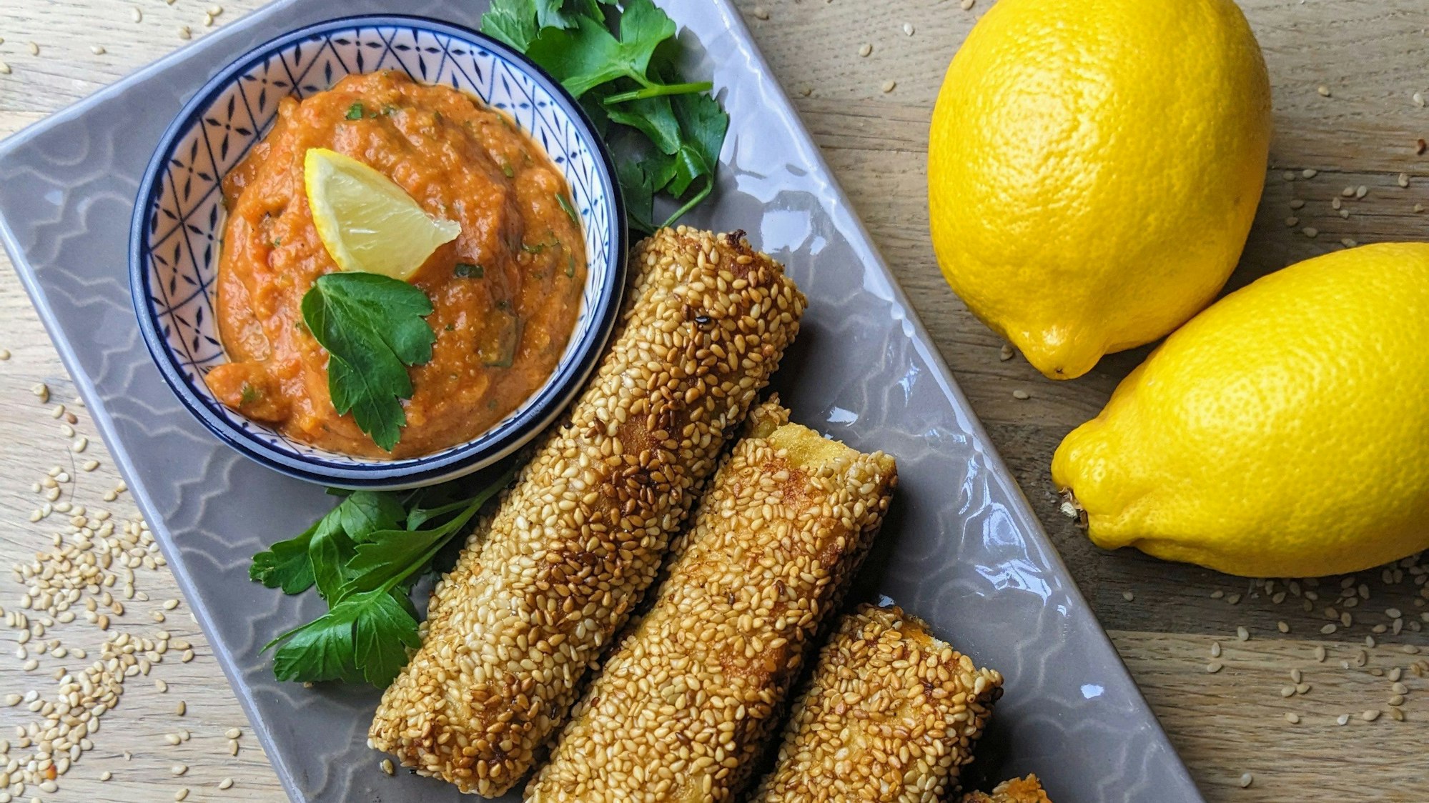 Fetakäse, Frischkäse und pürierte Paprika-Bohnen-Zwiebel-Tomatenmasse werden in plattgewalzten Toastbrotscheiben gewickelt, in Sesam gewälzt und in Butter goldbraun ausgebraten.