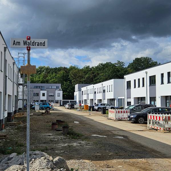 Weiße Häuser in Kubusform stehen entlang einer nicht unbefestigten Baustraße.