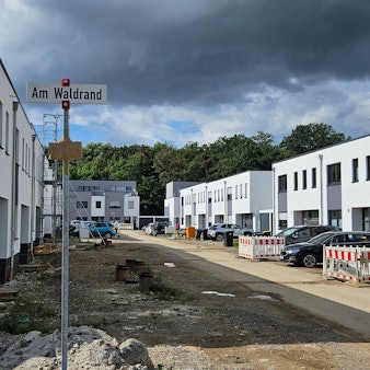 Weiße Häuser in Kubusform stehen entlang einer nicht unbefestigten Baustraße.