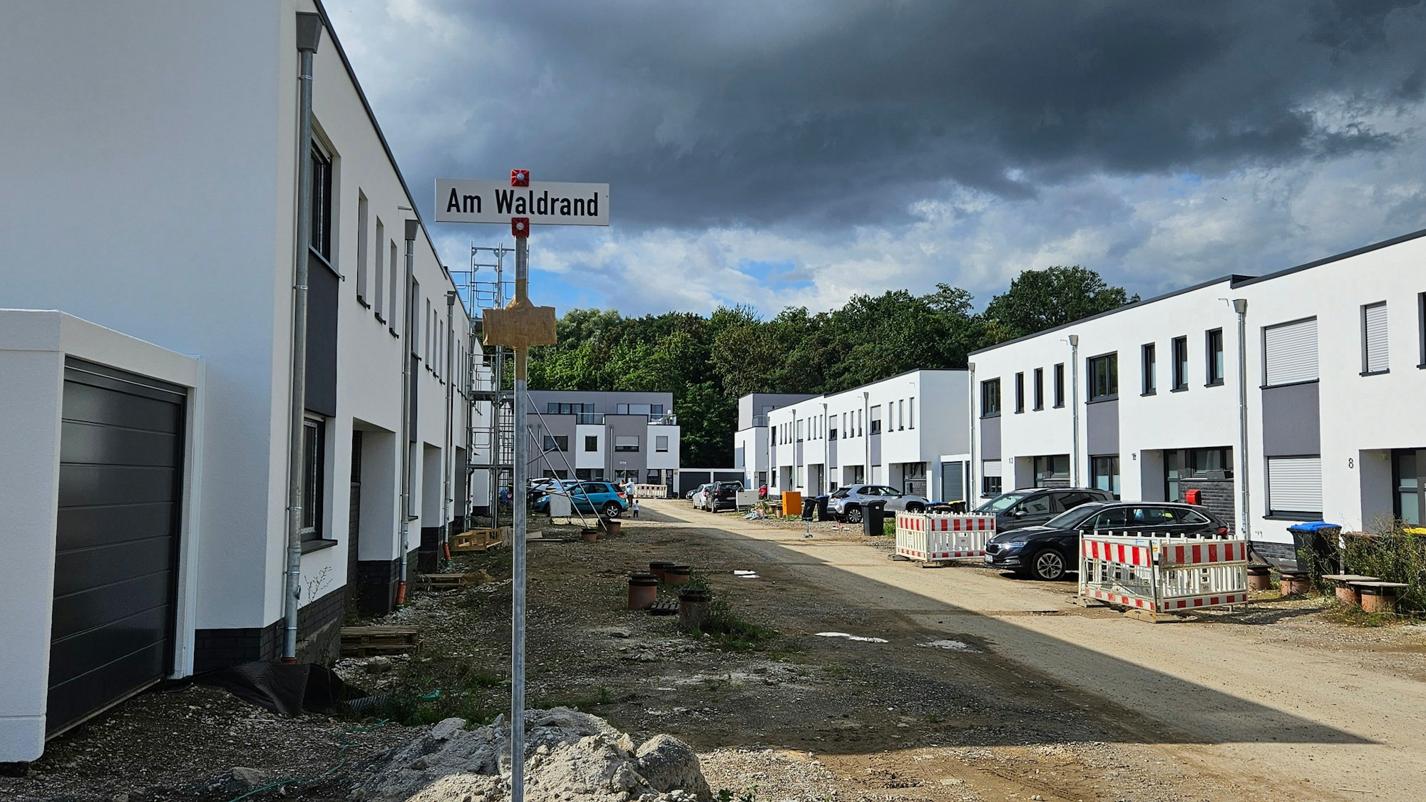 Weiße Häuser in Kubusform stehen entlang einer nicht unbefestigten Baustraße.