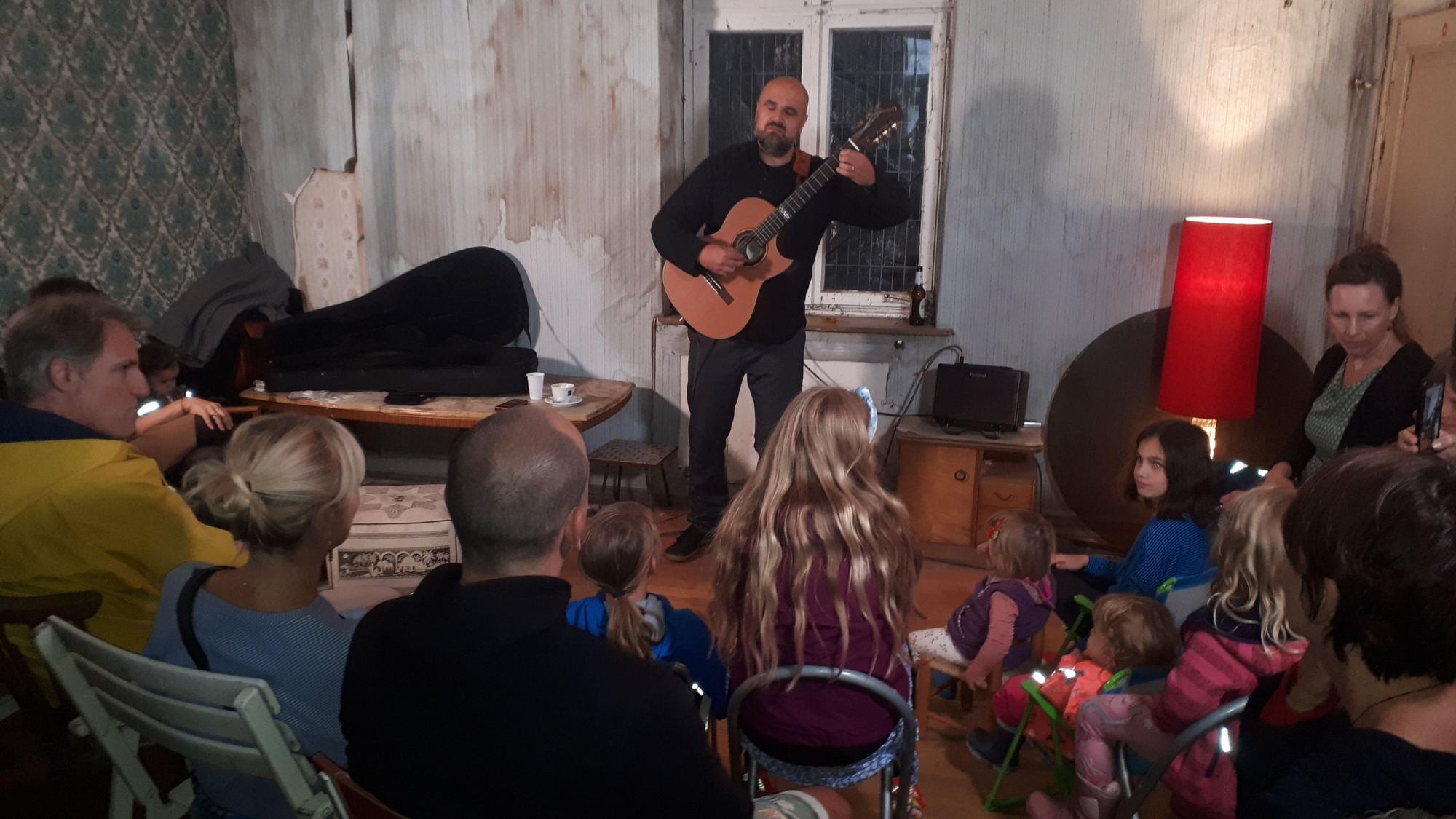 Ein Mann mit Gitarre singt, Zuschauer sitzen im Halbkreis um ihn herum.
