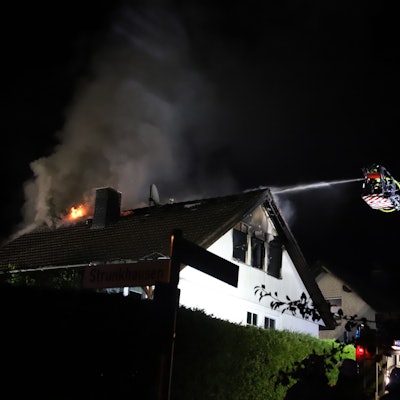 In einem frei stehenden Einfamilienhaus in Marienfeld ist in der Nacht vom 1. auf den 2. August das Dachgeschoss komplett ausgebrannt. Von der Drehleiter aus löschen Feuerwehrleute die Flammen.