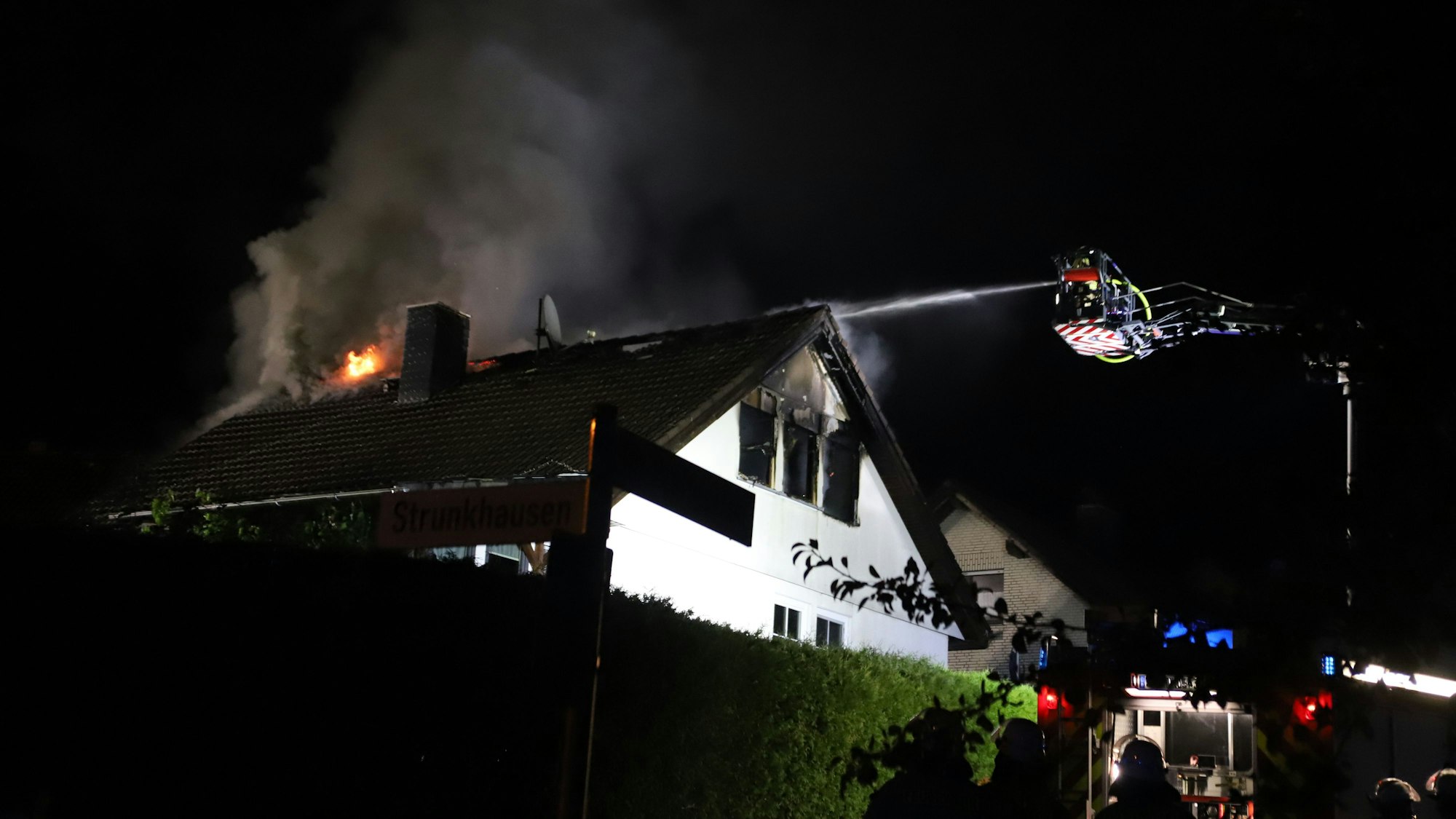 In einem frei stehenden Einfamilienhaus in Marienfeld ist in der Nacht vom 1. auf den 2. August das Dachgeschoss komplett ausgebrannt. Von der Drehleiter aus löschen Feuerwehrleute die Flammen.