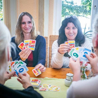 Im Psychosozialen Zentrum in Waldbröl sitzen die Gruppenleiterinnen Sarah Labisch (links) und Dagmar Titze an einem Tisch und spielen Karten mit psychisch beeinträchtigten Menschen, die einen geschützten Raum für den Austausch und Geselligkeit suchen.