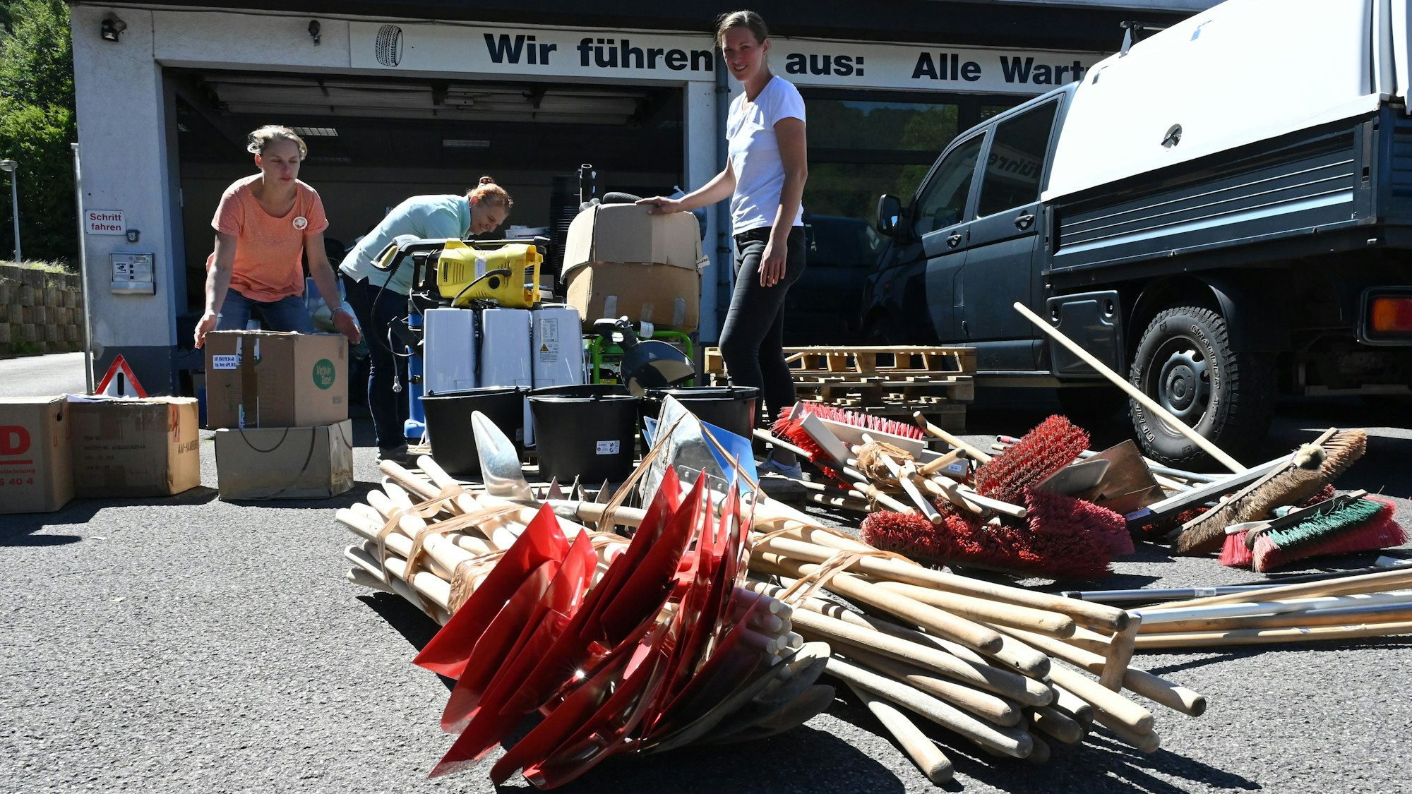 Drei Frauen, Rebecca Müller (v.r.), Tina Zavelberg-Pütz und Vera Church, stehen an zahlreichen Kisten. Im Vordergrund liegen viele Schaufeln und Besen auf dem Boden. Es sind Hilfsgüter für die Flutgebiete in Slowenien.