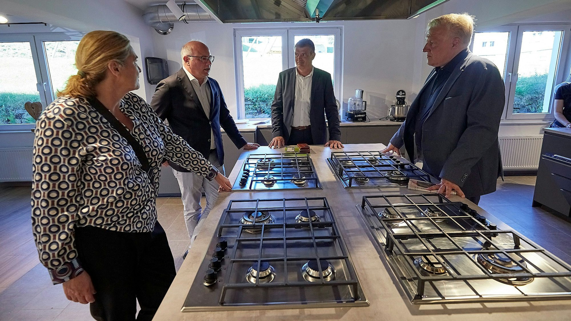 Oliver Suárez Cronauer (2.v.r.) Brit Possardt, Jochen Weiler (2.v.l.) und Wolfgang Spelthahn stehen um eine Kochinsel mit vier Gaskochfeldern.