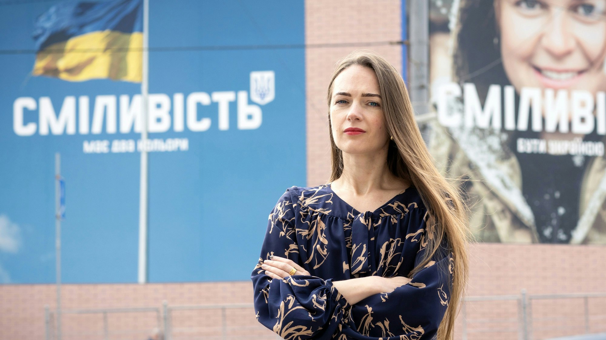 Olexandra Matwijtschuk steht vor einem Gebäude, auf dem ein Plakat mit der ukrainischen Flagge ist.