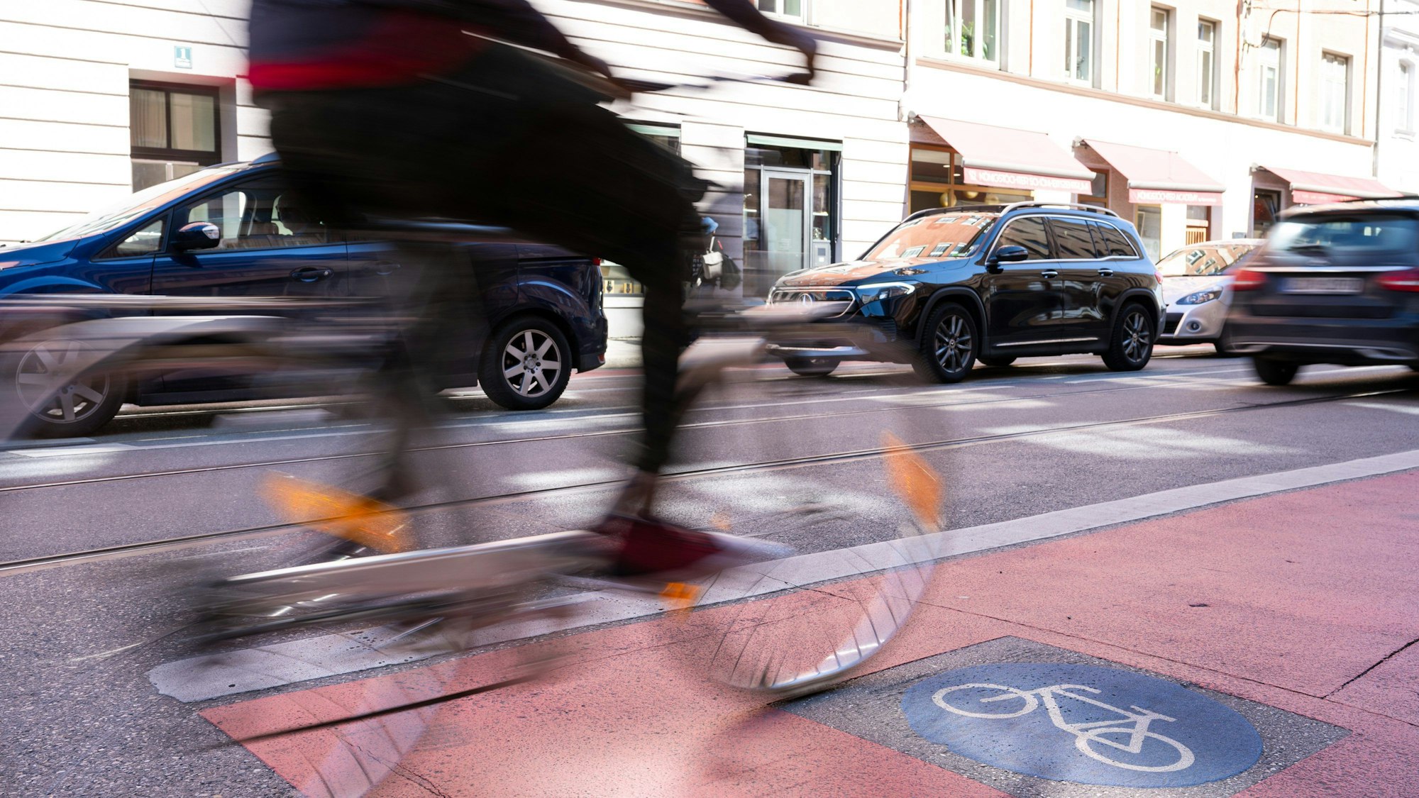 Ein Fahrradfahrer radelt auf einem Radweg neben fahrenden Autos.