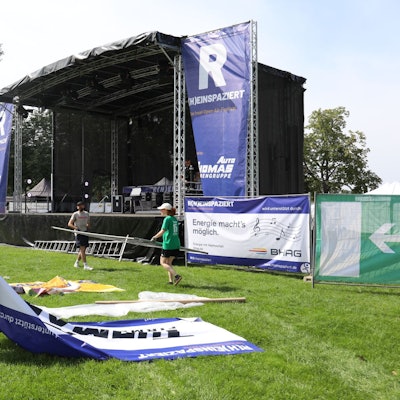 Helfer tragen Banner und Zaunelemente vor einer großen Bühne.