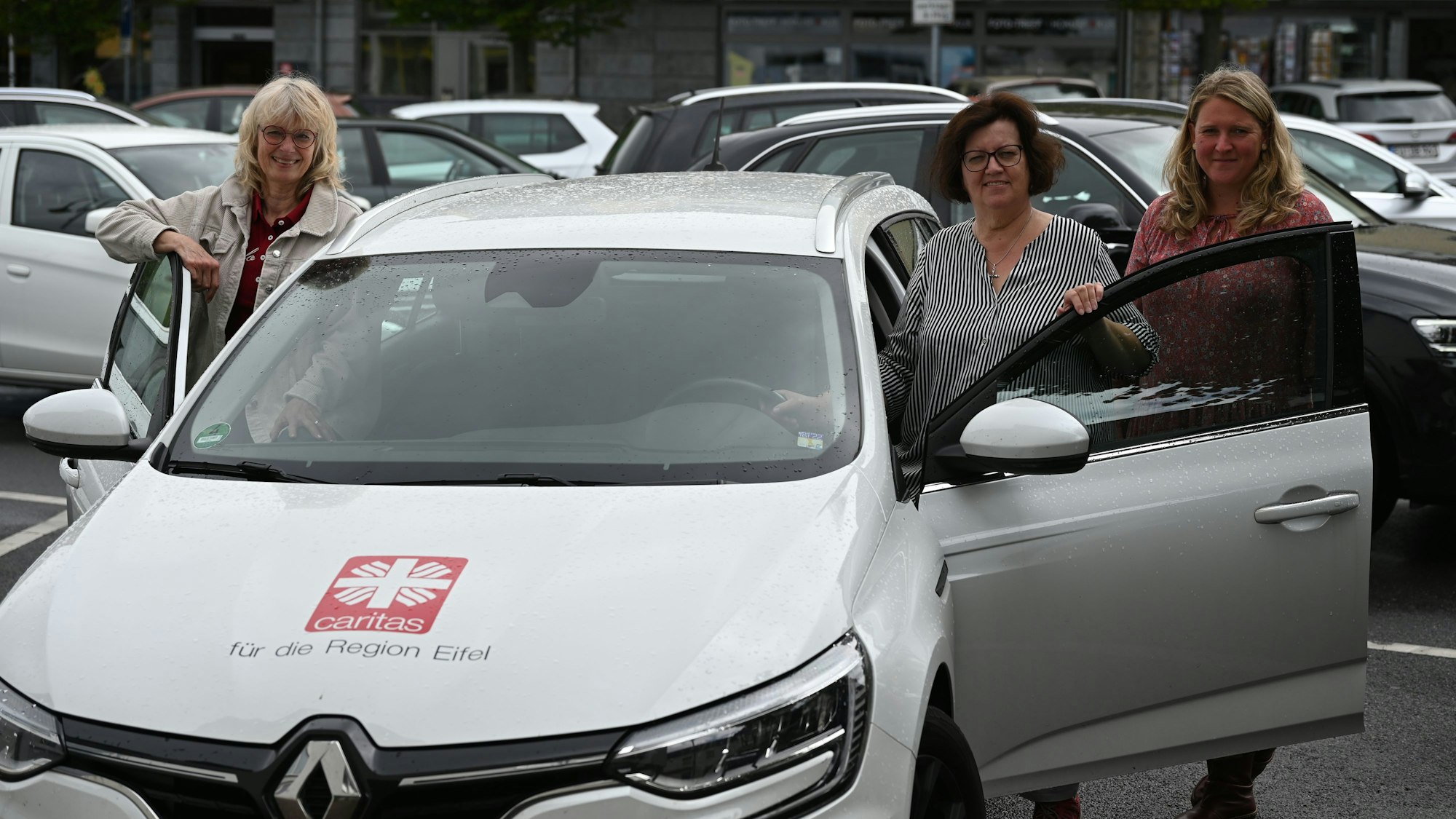 Die Caritas-Beraterinnen Annette Schäfer (l.) und Andrea Zens (M.) stehen an den geöffneten Türen eines der Autos, mit denen sie unterwegs sind. Bei ihnen steht Leiterin Soziale Arbeit bei der Eifeler Caritas, Christiane Kaufmann (r.)
