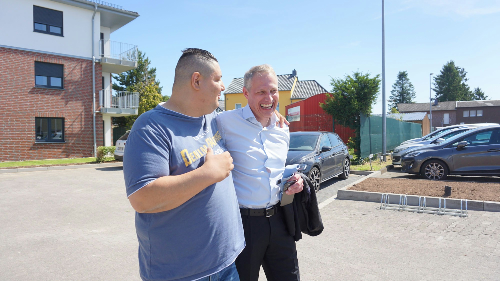 Kadir Aydin und Jürgen Abel laufen Arm in Arm über den Parkplatz.