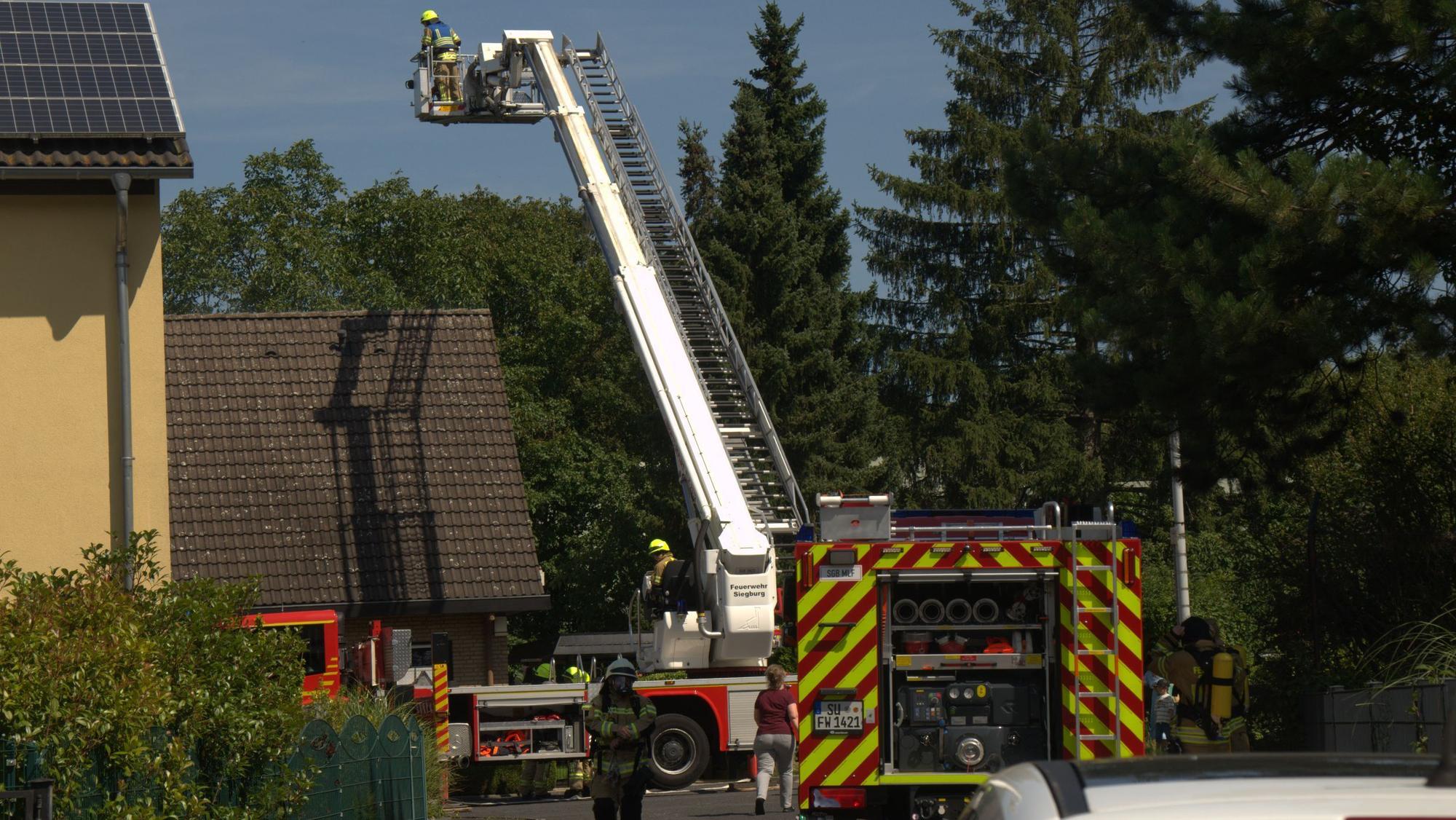 Die Feuerwehr hat eine Drehleiter ausgefahren, der Korb steht hoch über einem Einfamilienhaus.