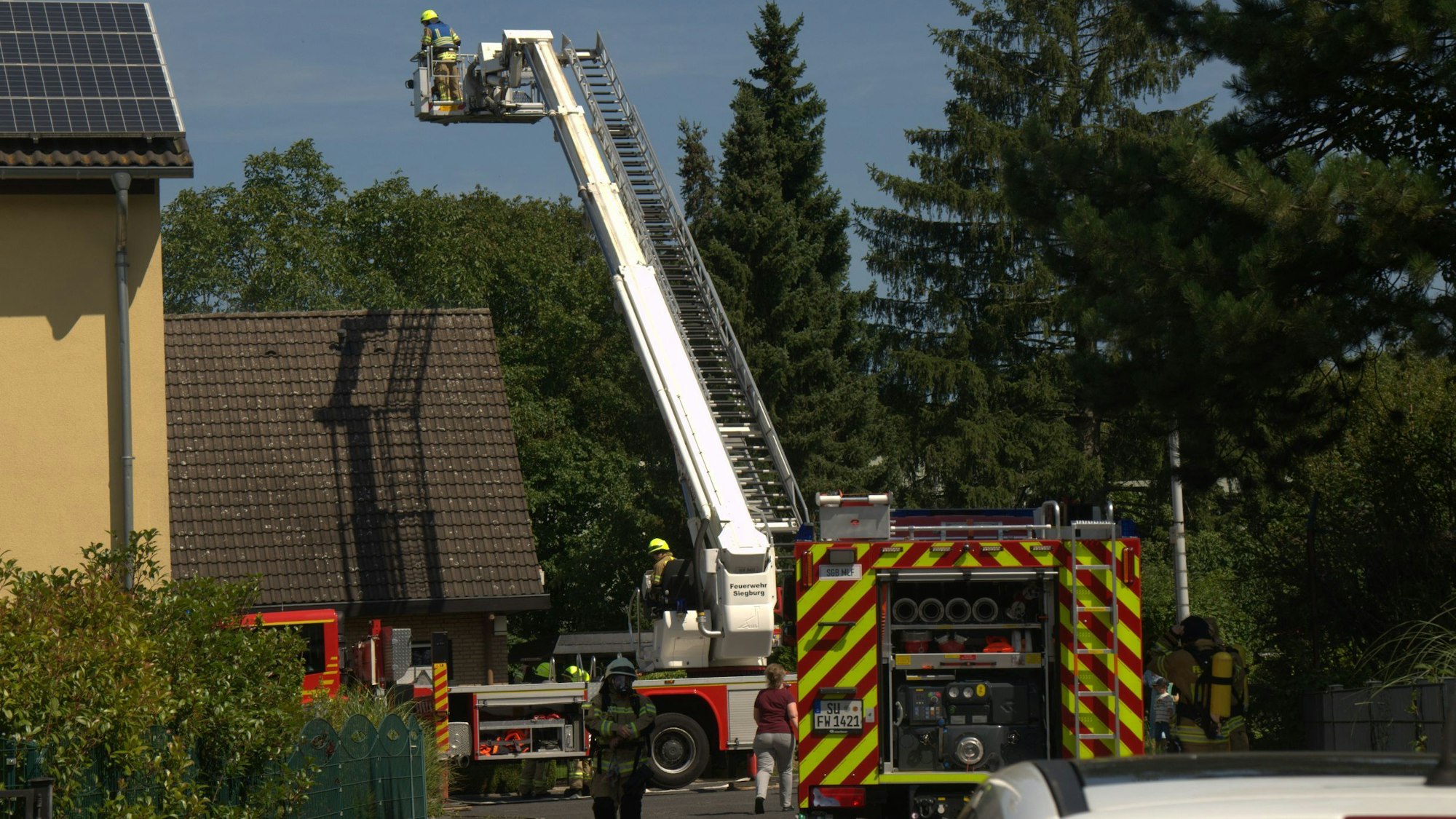 Die Feuerwehr hat eine Drehleiter ausgefahren, der Korb steht hoch über einem Einfamilienhaus.