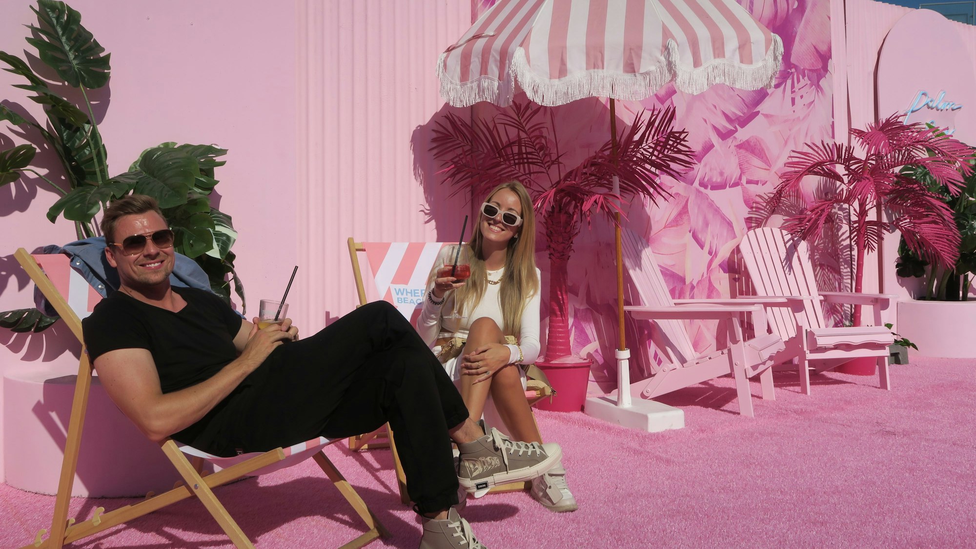 Zwei Menschen sitzen auf rosafarbenen Liegestühlen.