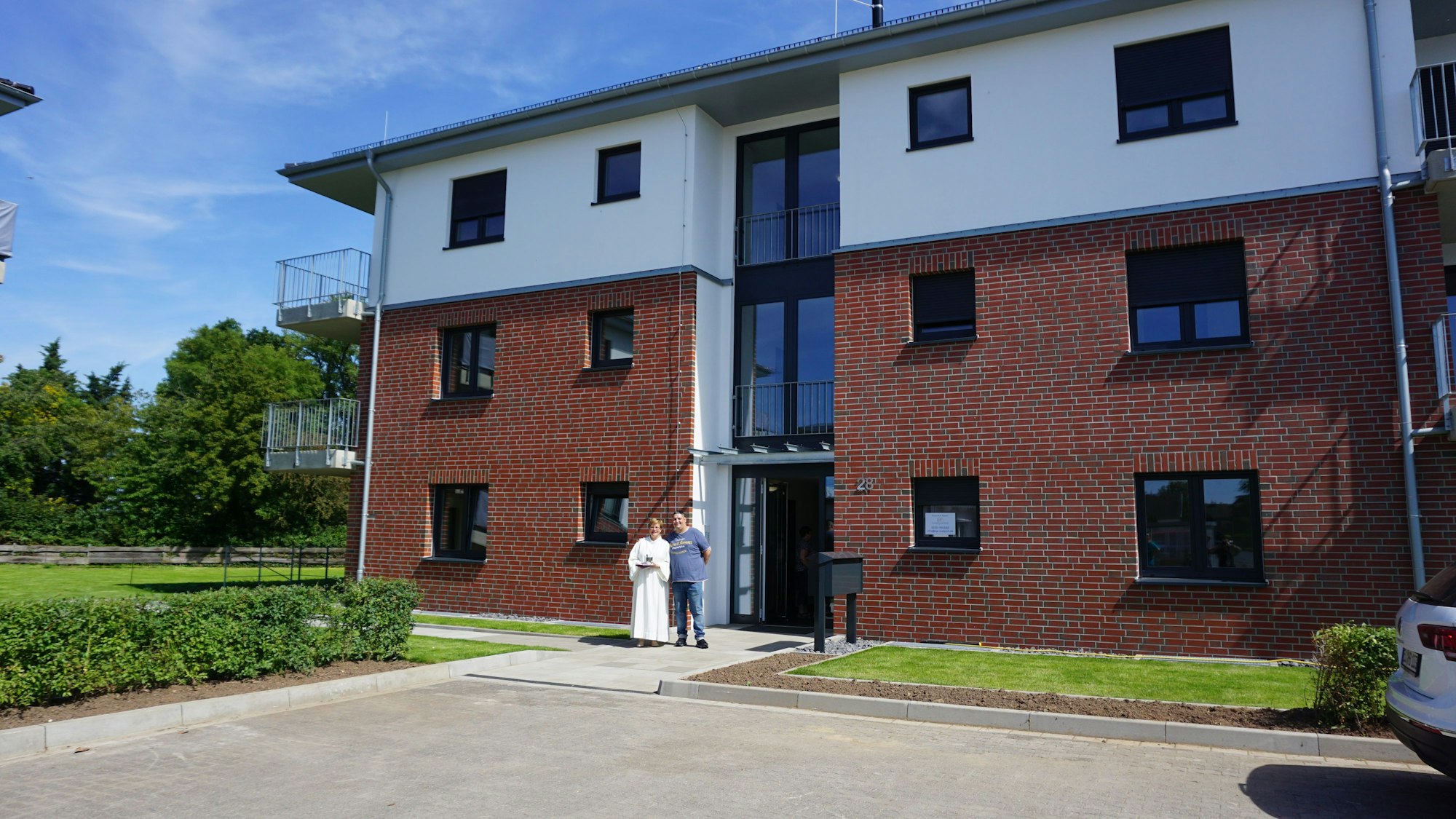 Kadir Aydin und Dorothea Grimm stehen vor einem dreistöckigen Neubau mit Balkonen.