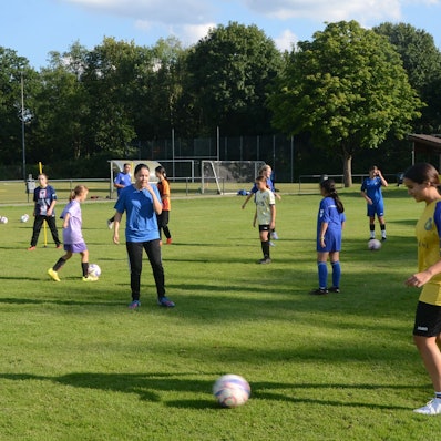 Auf einem Trainingsplatz machen Mädchen Fußball-Übungen. Sie tragen blaue, gelbe und weiße Trikots.