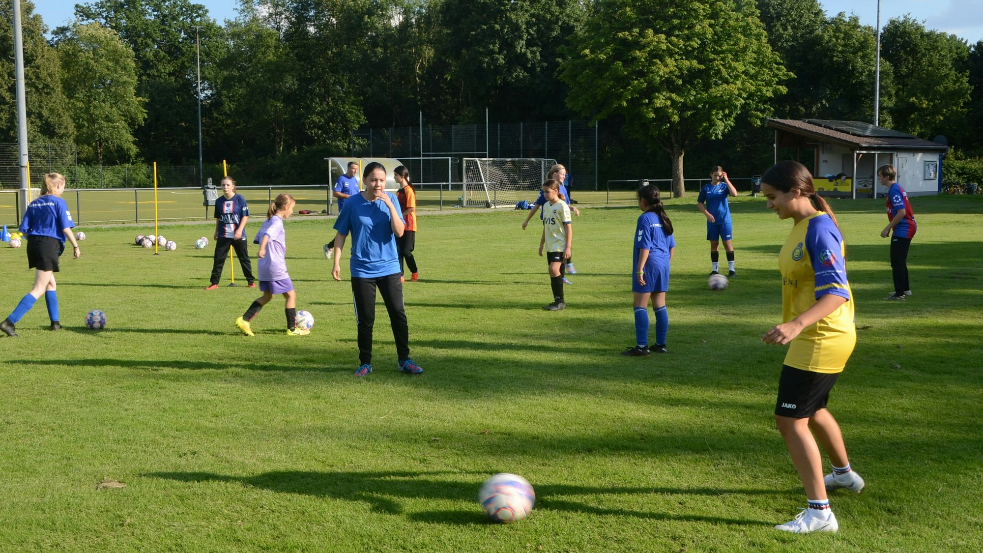 Auf einem Trainingsplatz machen Mädchen Fußball-Übungen. Sie tragen blaue, gelbe und weiße Trikots.