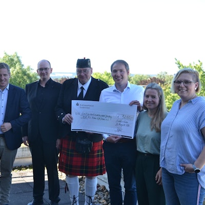 Eine Gruppe Menschen steht zusammen. Sie halten zwei große Schecks, auf denen jeweils 6250 Euro an Spenden für Fluthilfeorganisationen ausgewiesen sind.