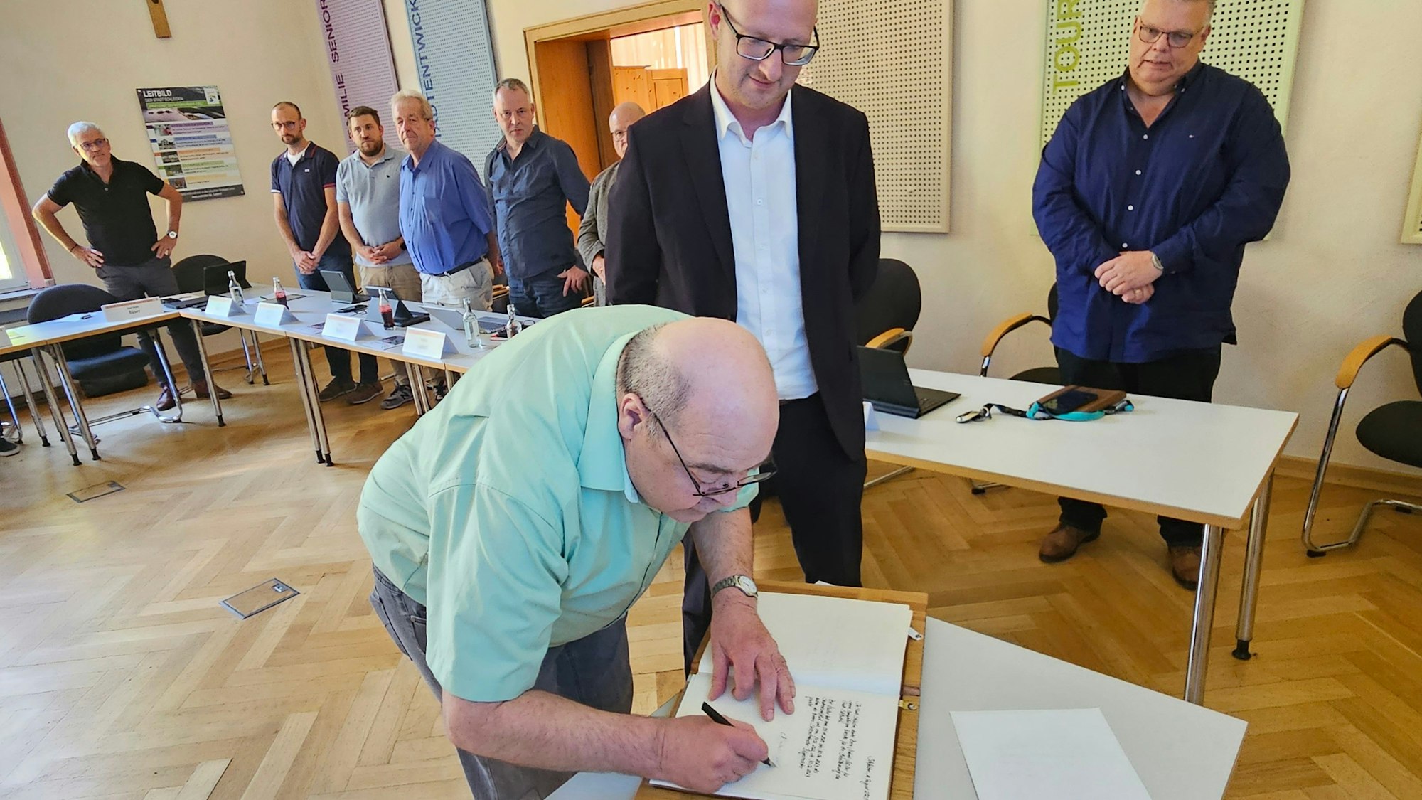 Norbert Müller steht an einem Tisch und trägt sich ins Goldene Buch der Stadt Schleiden ein. Bürgermeister Ingo Pfennings steht neben ihm und schaut zu, ebenso weitere Politiker.