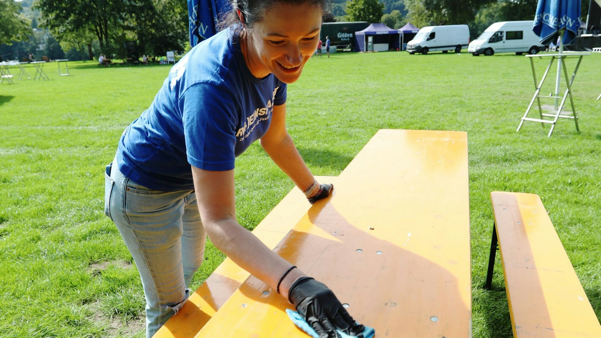 Eine junge Frau im blauen T-Shirt wischt einen Tisch sauber.