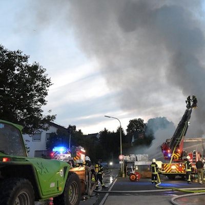 Rauchwolken und Flammen schlagen aus einem Gebäude in den Abendhimmel. Die Feuerwehr löscht den Brand.