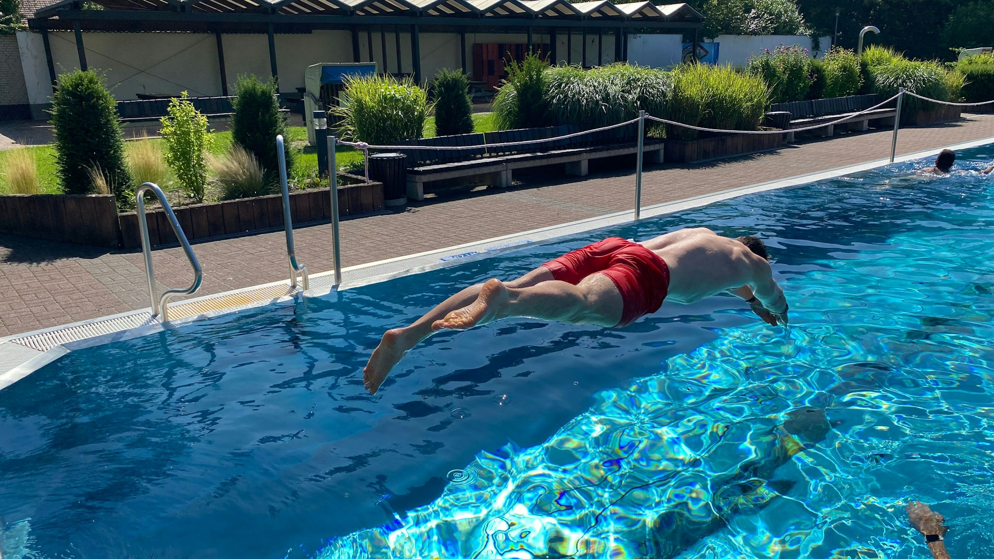 Ein Mann in roter Badehose macht einen Kopfsprung ins Wasser.