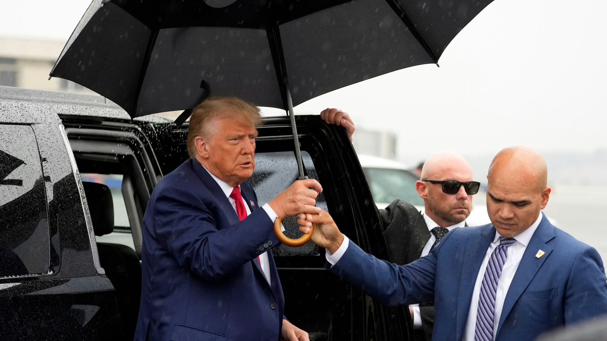 Walt Nauta (r), Leibwächter des Ex-US-Präsidenten Trump, reicht Donald Trump (l), ehemaliger Präsident der USA, einen Regenschirm, bevor er am Ronald Reagan Washington National Airport eine Rede hält.