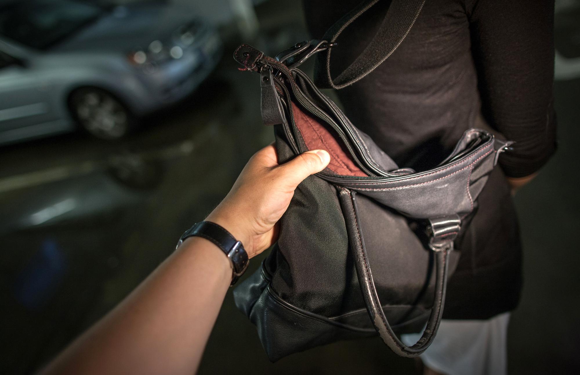 Ein Hand greiftnach einer Geldbörse in einer Damenhandtasche.