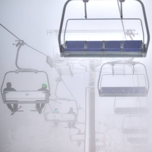 Wintersportler fahren mit einem Sessellift über eine künstlich beschneite Piste. Es ist neblig. (Symbolbild)