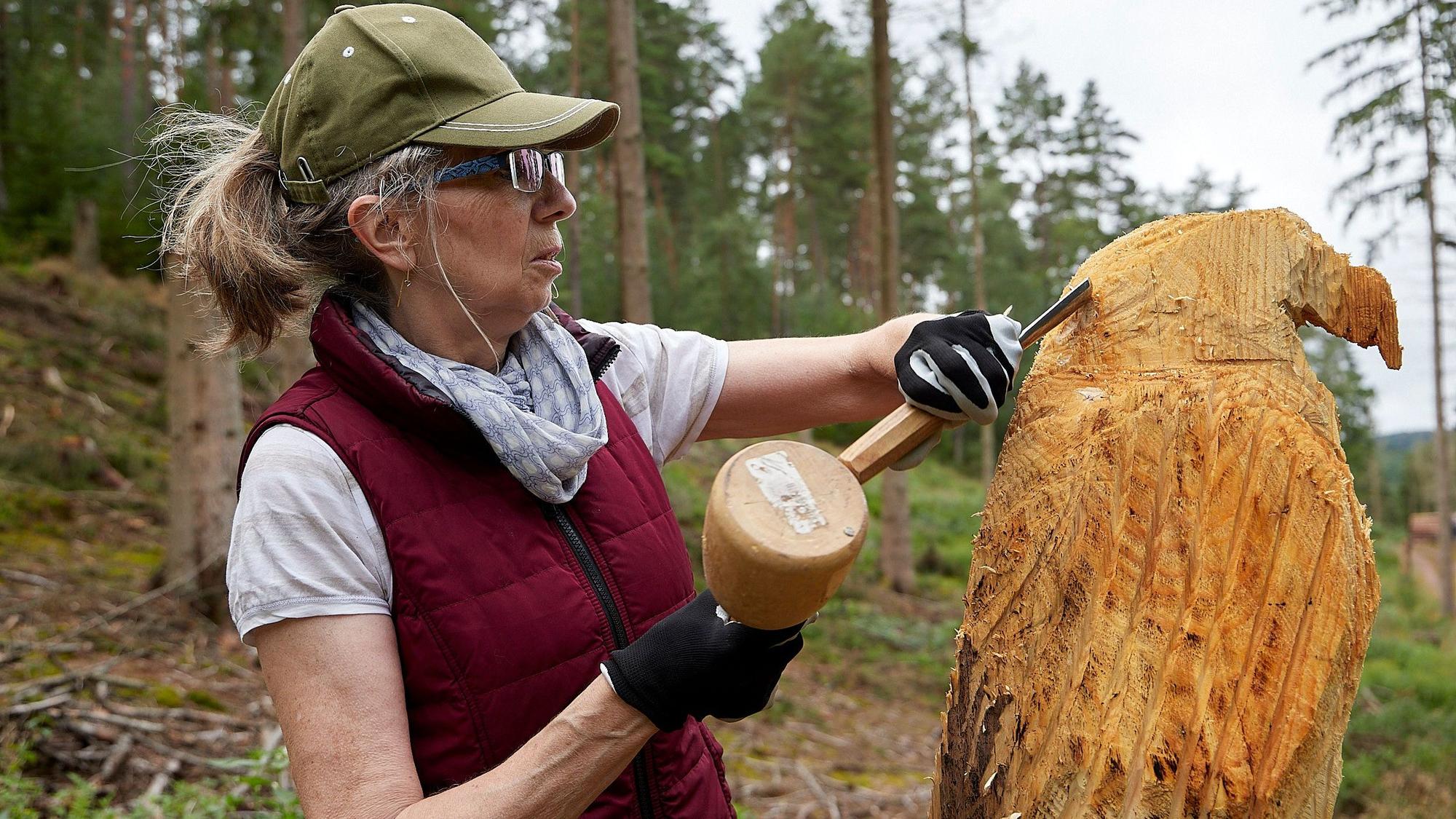 Vera Philipp hält Hammer und Meißel in der Hand und arbeitet an einer Holzfigur, die bereits aussieht wie ein Adler.