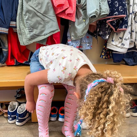 Ein Kita-Kind sitzt auf einer Bank und zieht sich Schlappen an.