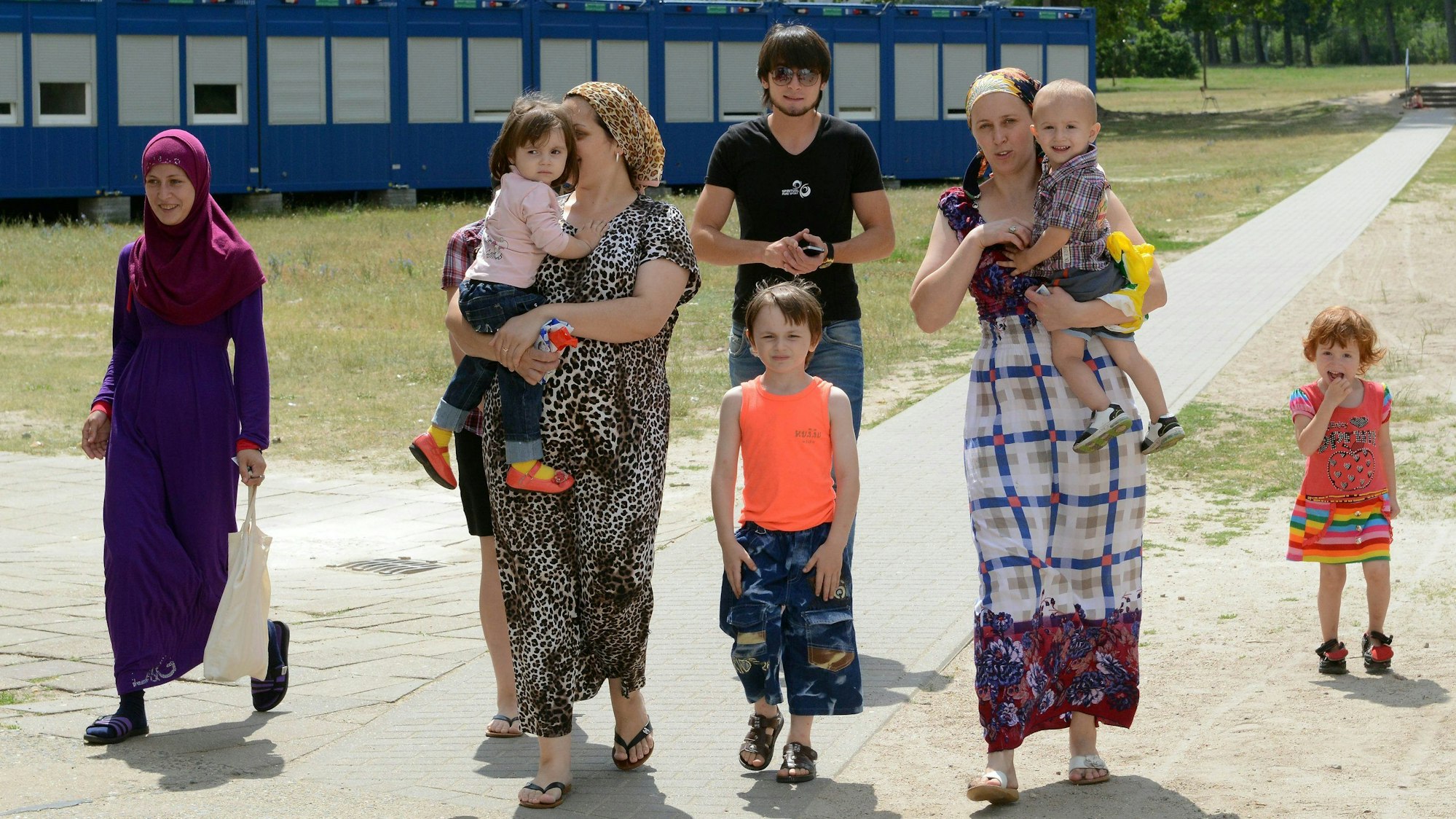 Asylbewerber aus der russischen Födereration gehen am 17.07.2013 in Eisenhüttenstadt (Brandenburg) in der Erstaufnahmeeinrichtung für Flüchtlinge an Unterbringungscontainern vorbei. Knapp 700 Flüchtlinge leben derzeit in dem Heim das ursprünglich für 500 Asylsuchende ausgelegt war. Foto: Bernd Settnik/dpa +++(c) dpa - Bildfunk+++