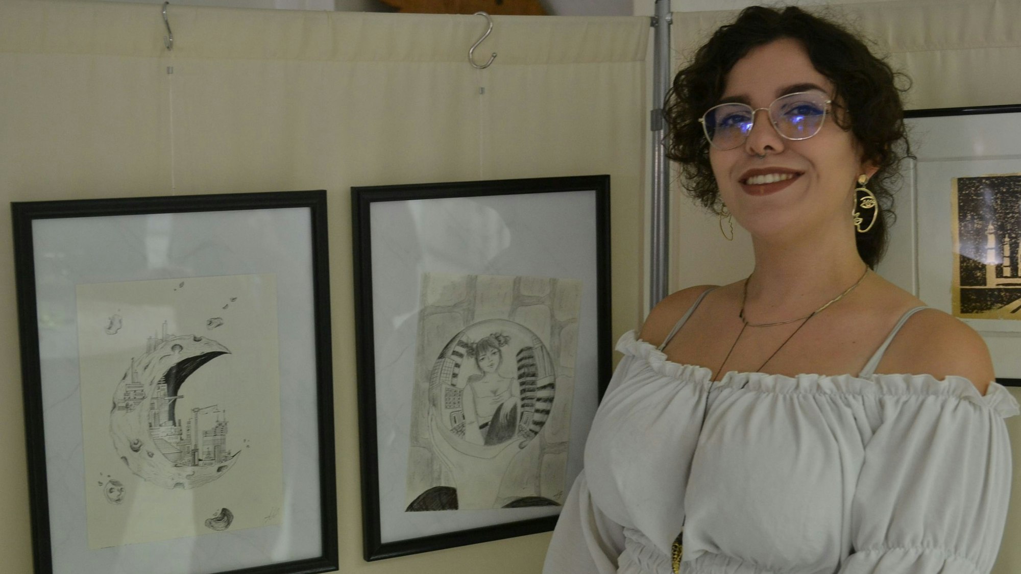 Das Bild zeigt Angela Neuhaus, die neben ihren zwei Bleistiftzeichnungen steht. Die Zeichnungen zeigen das Innere des Mondes.