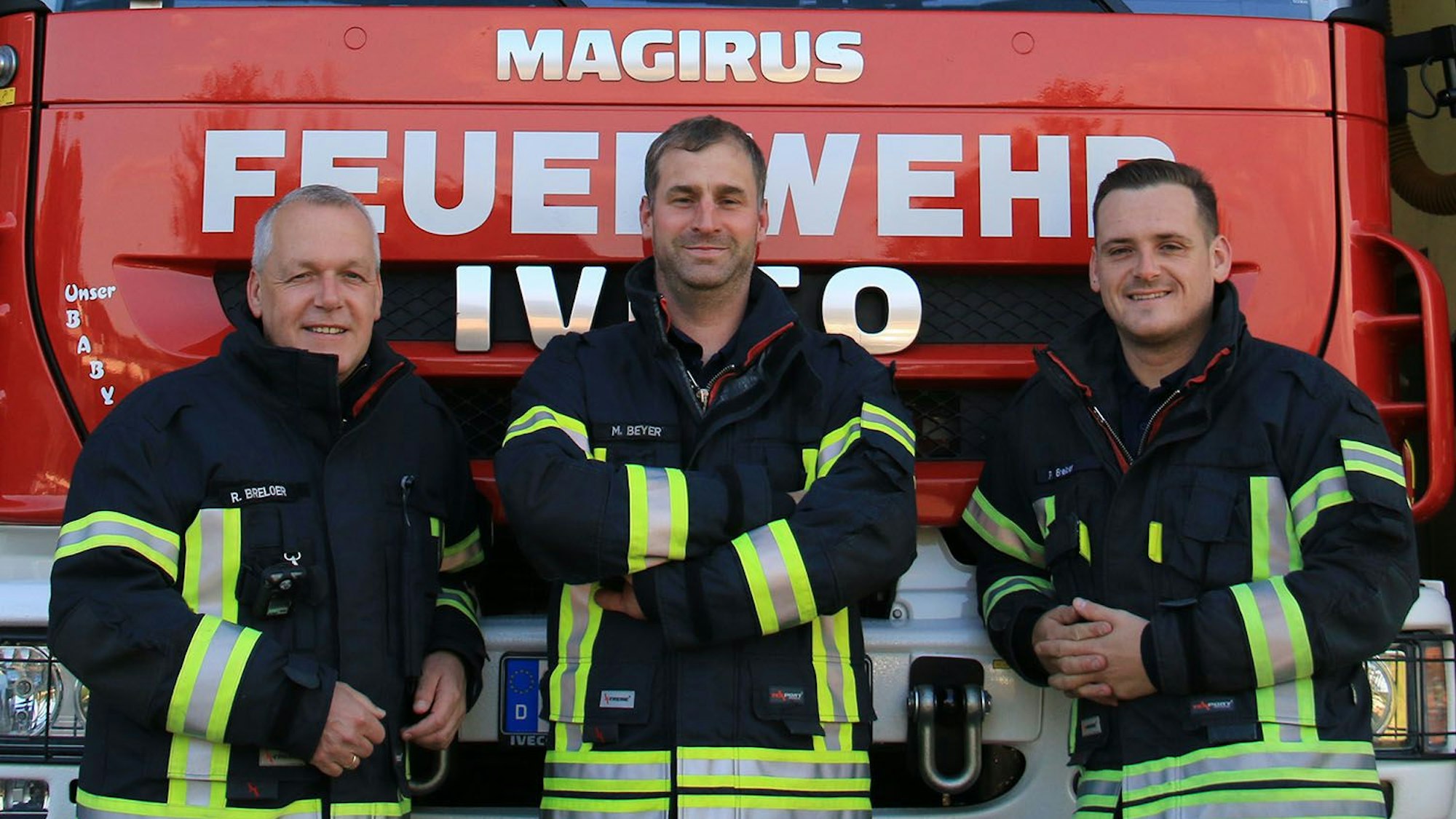 Drei Feuerwehrmänner in Einsatzkleidung stehen vor einem Einsatzfahrzeug.