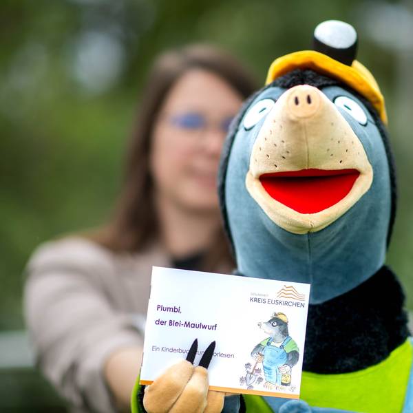 Das Bild zeigt die Handspielfigur Plumbi, die ein kleines Buch in die Kamera hält.
