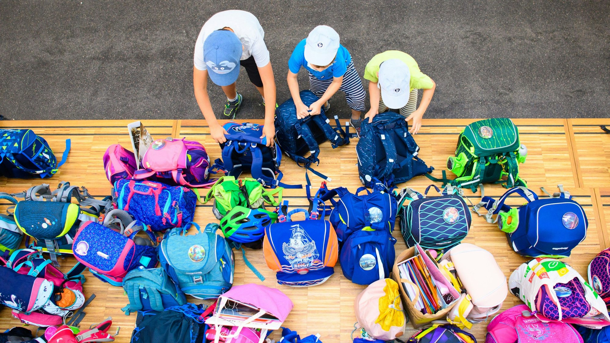 Drei Erstklässler stellen in einer Grundschule ihre Schultaschen ab.