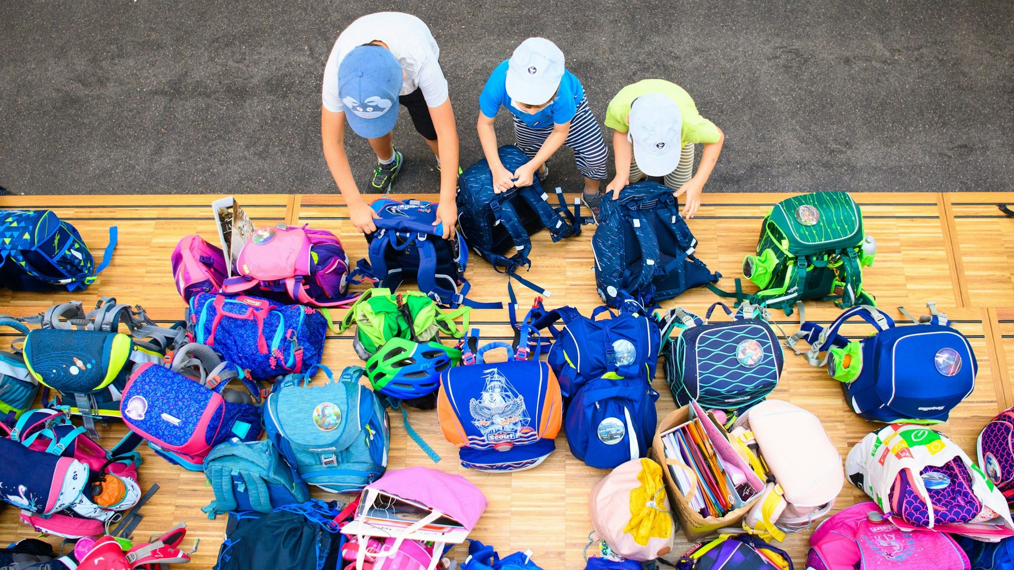 Drei Erstklässler stellen in einer Grundschule auf einem Podest ihre Schultaschen ab.