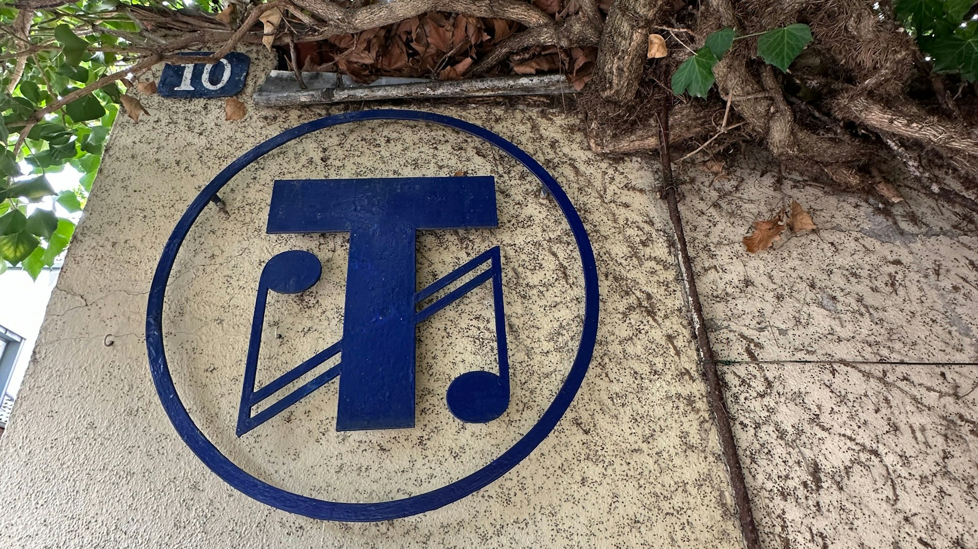 An einer Hauswand prangt ein rundes Logo mit zwei miteinander verwobenen Noten darin.