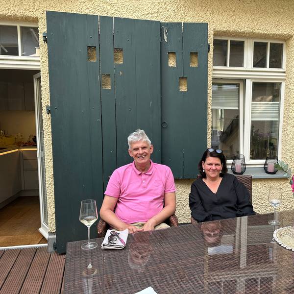 Ein Paar sitzt auf einer Dachterrasse an einem Holztisch.