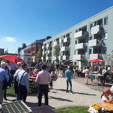 Mehrere Menschen stehen vor dem neuen Wohnhaus an der Ecke Josefine-Clouth-Straße/Xantener Straße.