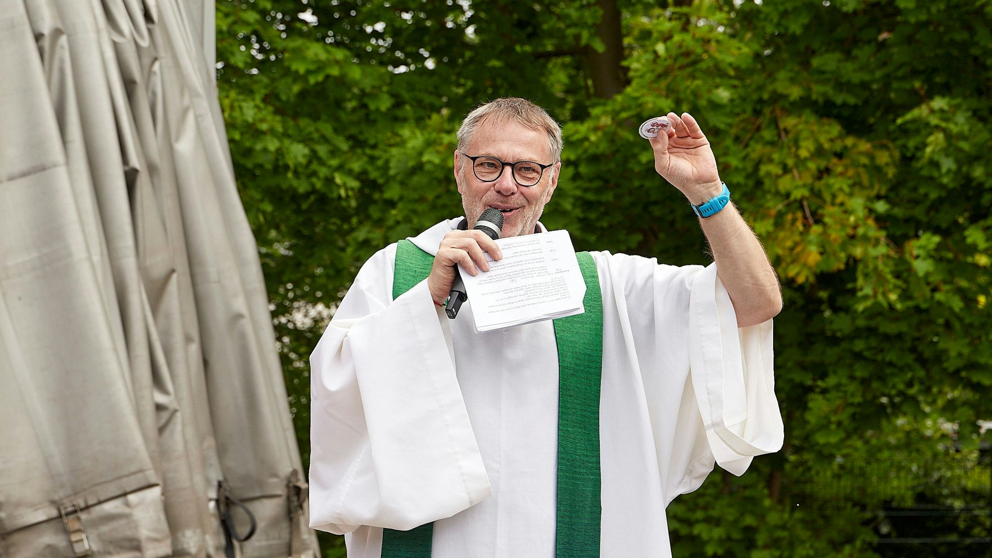 Pfarrer Hardy Hawinkels hält bei seiner Predigt ein Mikrofon und Notizen in der Hand.