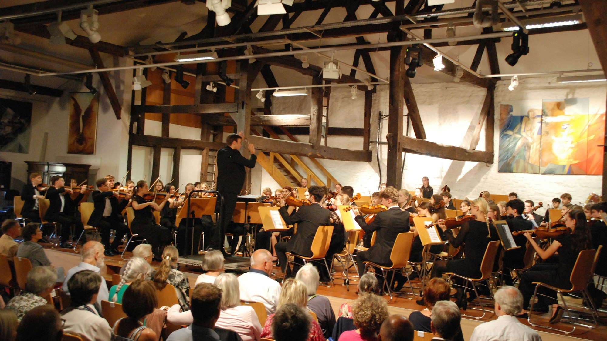 Zu sehen sind das Orchester mit dem Dirigenten Vitali Alekseenok und ein Teil der Zuhörer.