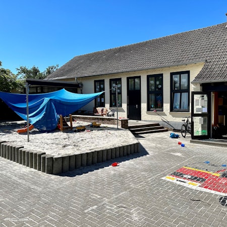 Das Außengelände einer Kita mit Sandkasten und Pflastermosaik.