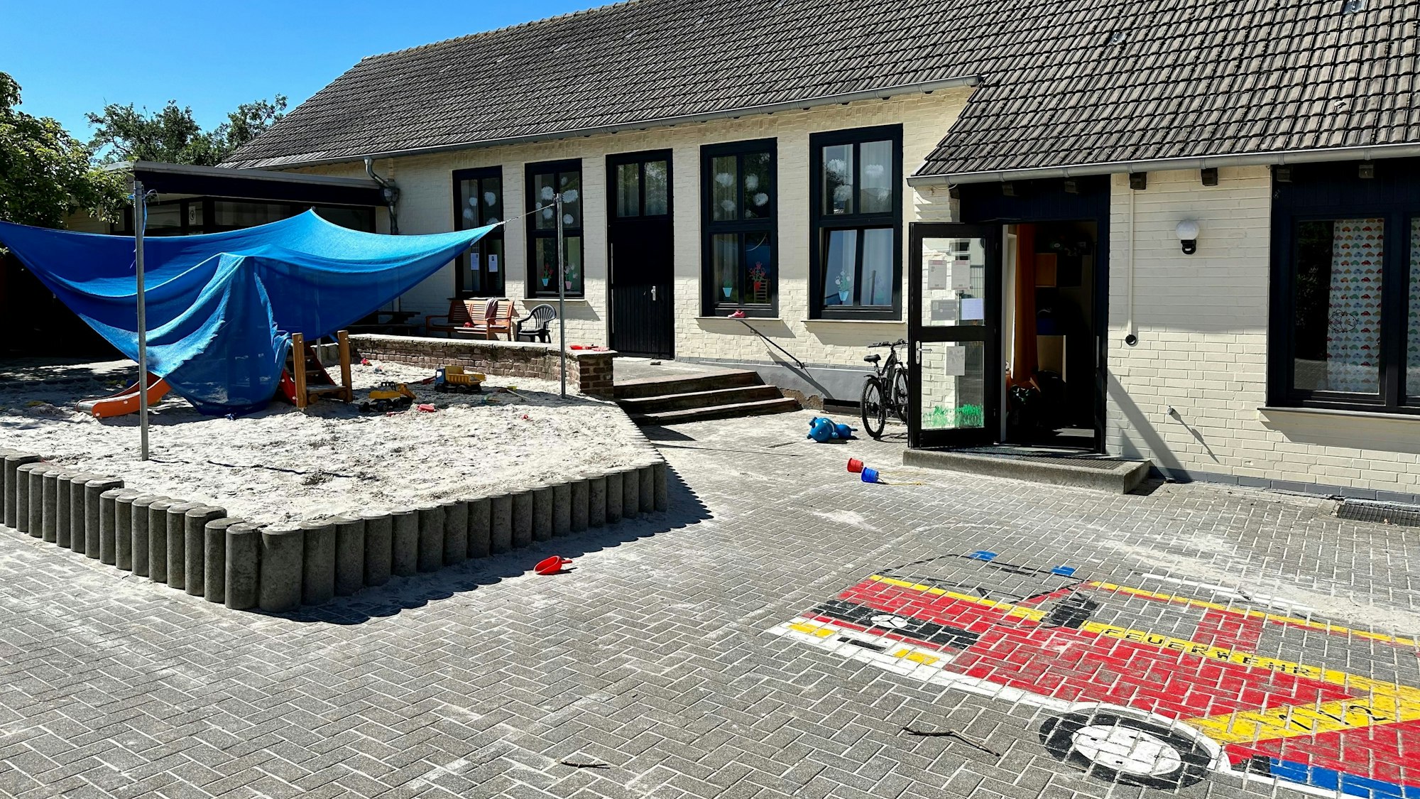 Das Außengelände einer Kita mit Sandkasten und Pflastermosaik.