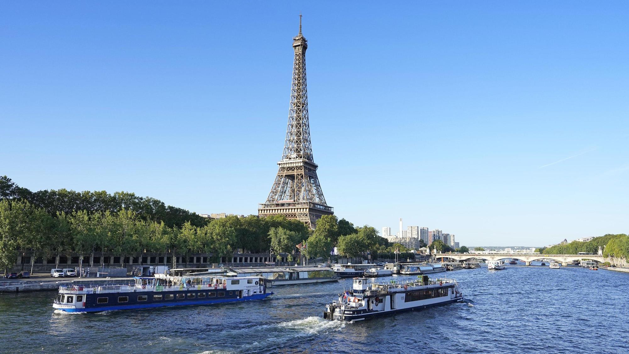 ARCHIV - 17.07.2023, Frankreich, Paris: Ein Boot und ein Lastkahn fahren vor dem Eiffelturm auf der Seine während eines Tests für die Eröffnungsfeier der Olympischen Spiele 2024 in Paris.