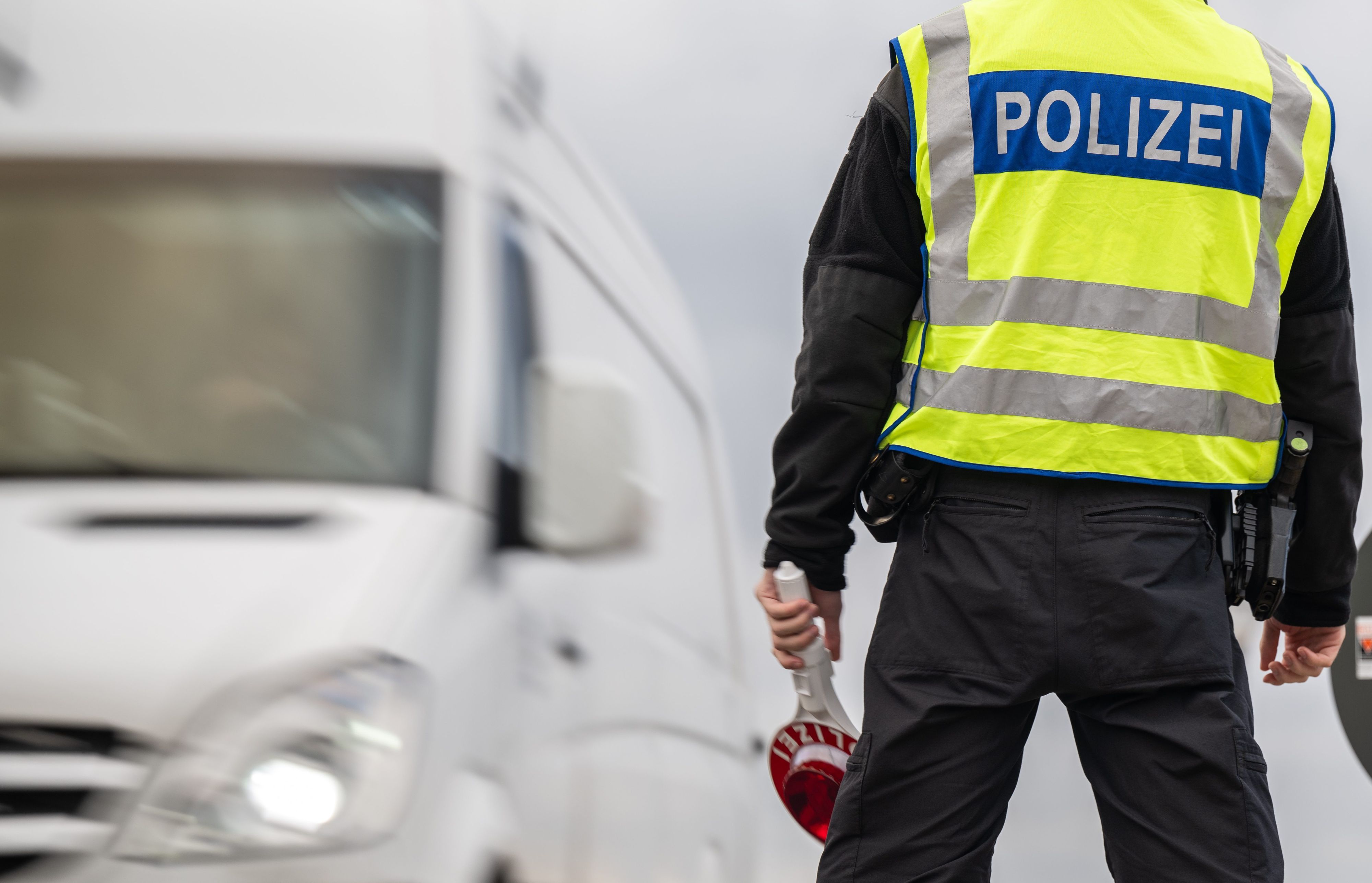 Ein Transporter passiert einen Polizisten mit Haltekelle in der Hand. (Symbolbild)