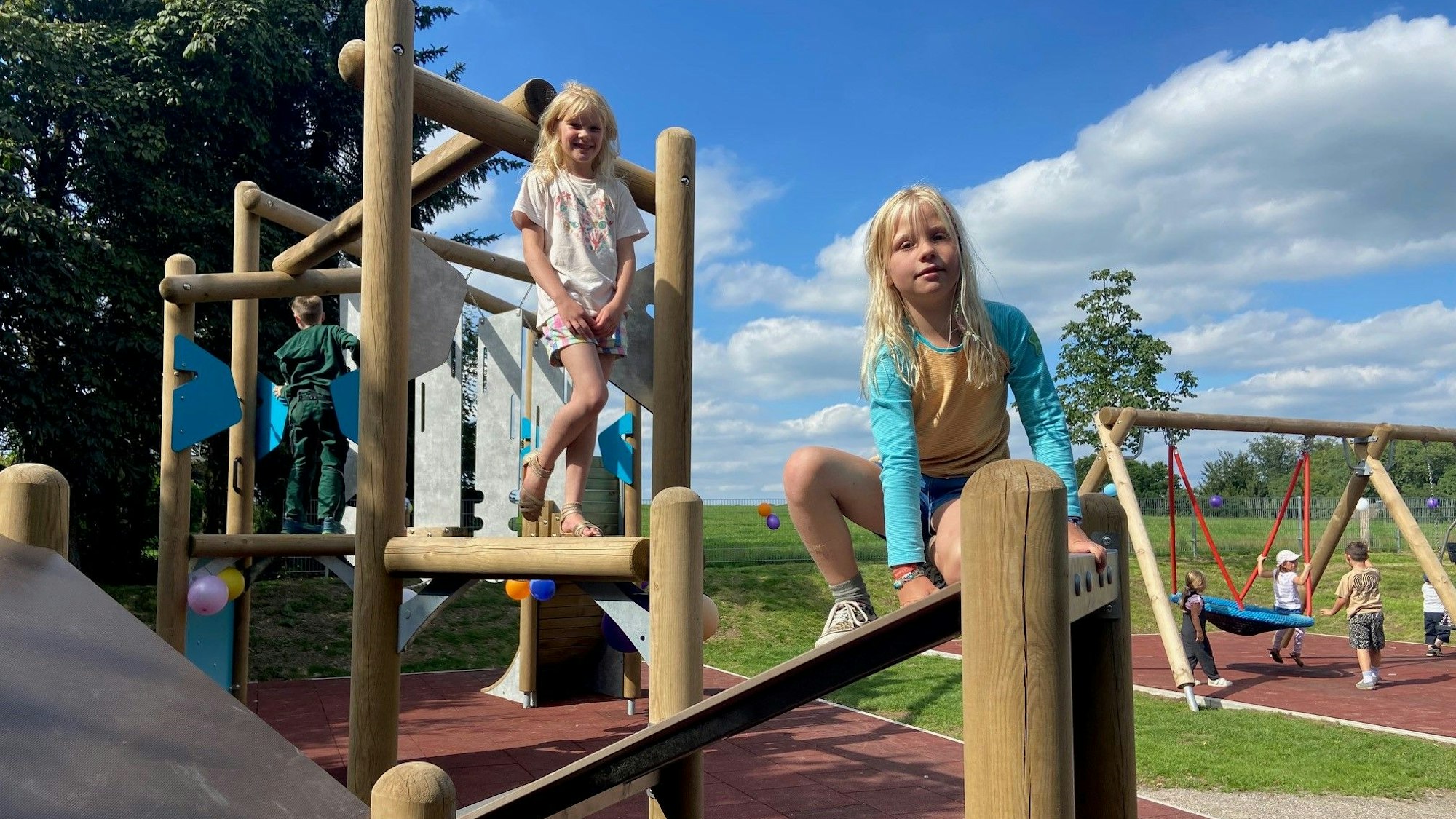 Zwei Mädchen klettern auf einem neuen Klettergerüst eines Spielplatzes.
