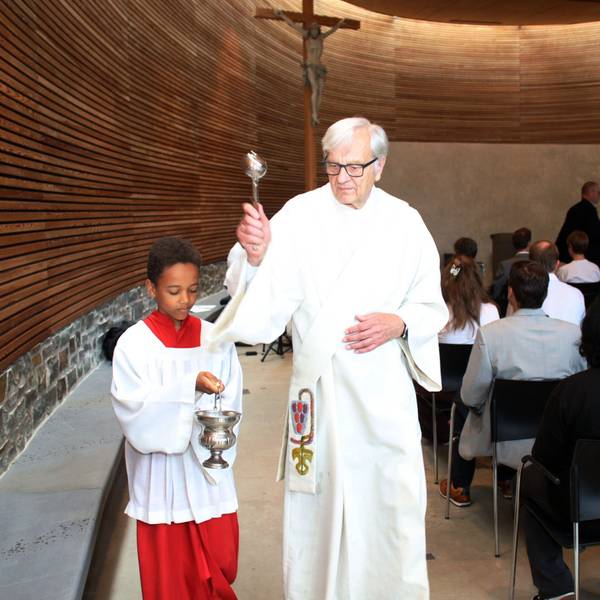 Diakon Dr. Ulrich Günzel segnet die Schulkapelle des St.-Angela-Gymnasiums ein. Neben ihm hält ein Messdiener ein Weihwasserfässchen.